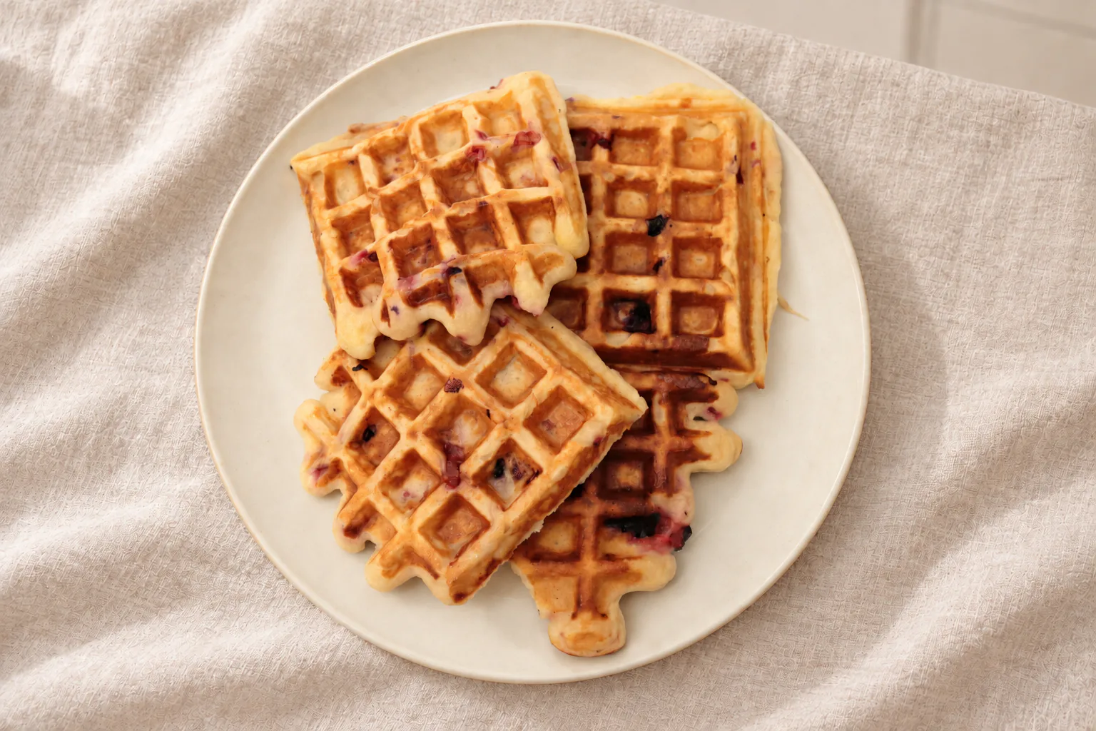 Golden gluten-free curd cheese waffles with berries on an ivory ceramic plate
